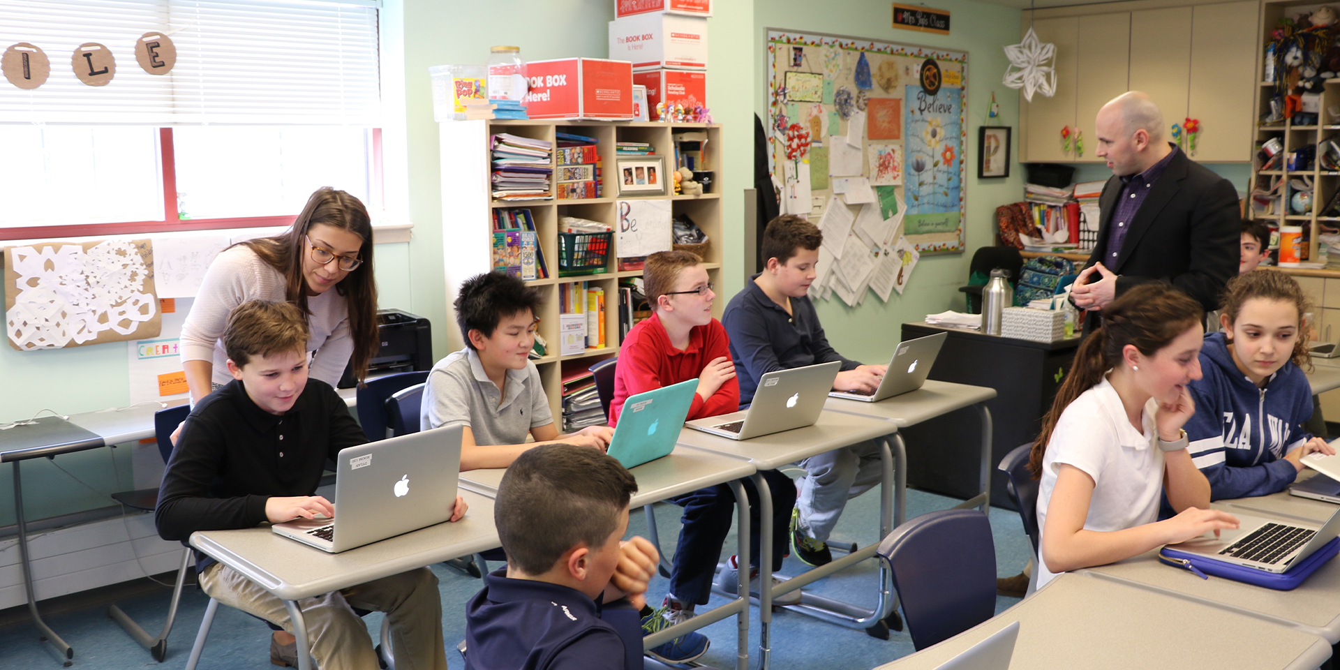 Two teachers help students with laptops in classroom