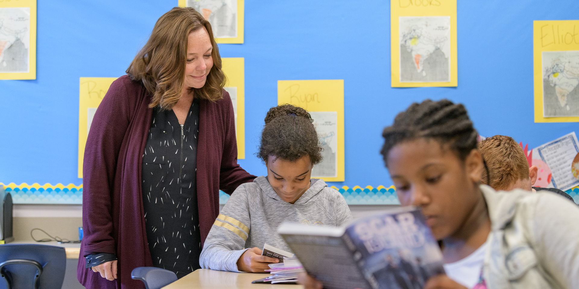 Teacher looks over student's shoulder as she reads book
